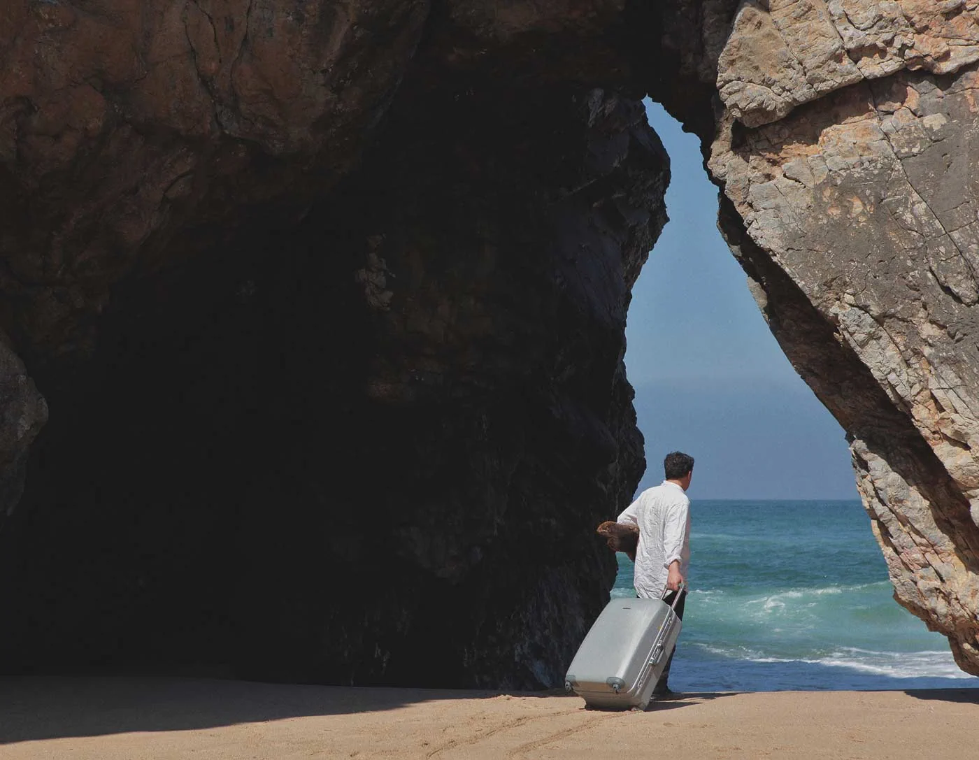 Photographic artwork showing a traveller by a rocky seaside opening, used for Other Spaces at MACAM