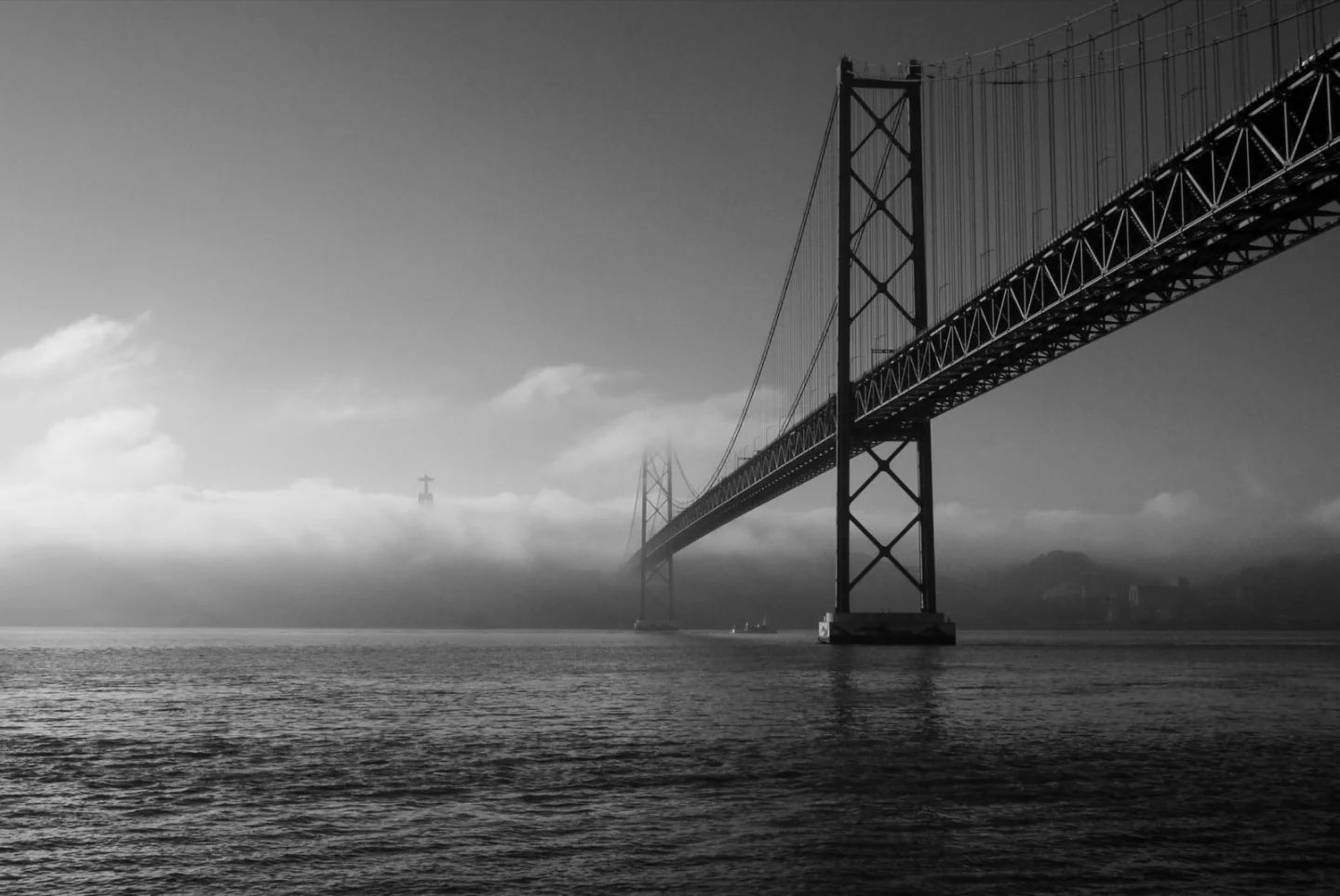 An original black-and-white photograph of the 25 de Abril bridge over the Tagus through low clouds.