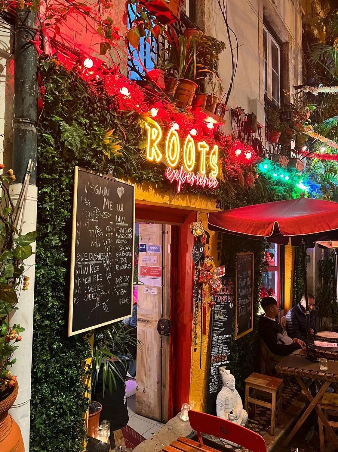 The illuminated Roots Experience storefront on Rua da Silva