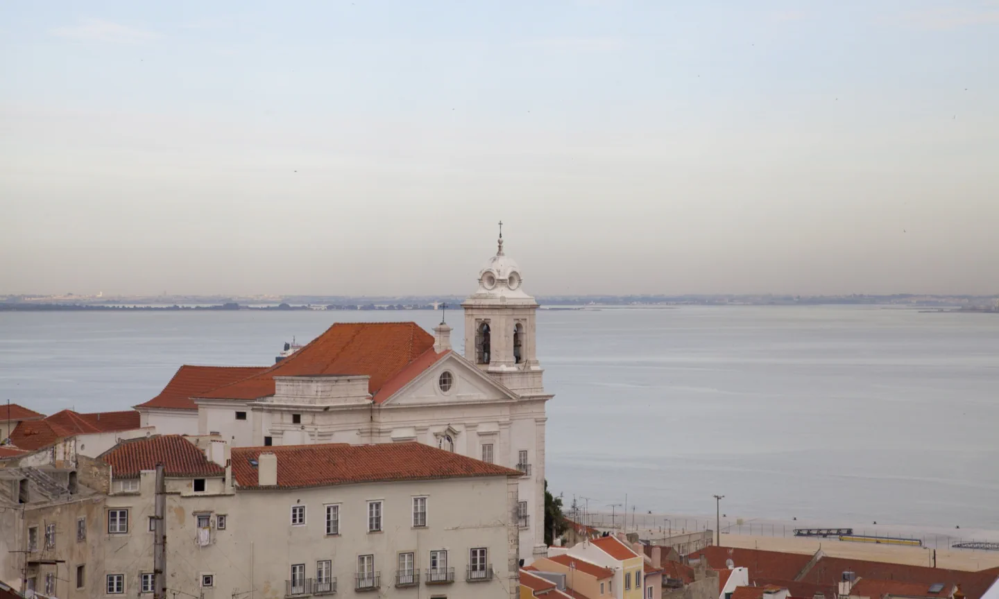 Igreja de Santo Estêvão and Alfama's red-tiled roofs overlooking the Tagus in soft evening light, seen from Santa Luzia.